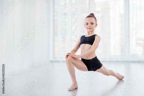 Flexible child, beautiful little gymnast girl doing gymnastic exercises or exercising in fitness class