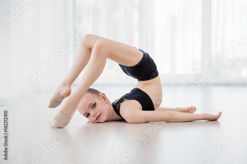 Flexible child, beautiful little gymnast girl doing gymnastic exercises or exercising in fitness class