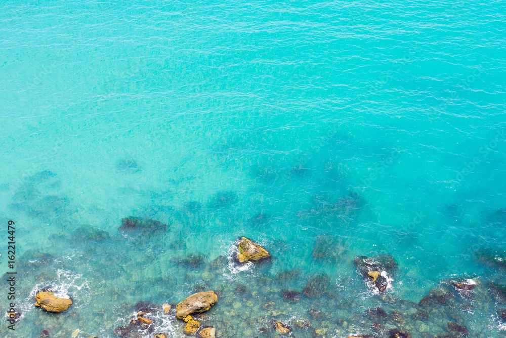 Sea Rocks And Wave Splashes With Vibrant Blue Water Background WIth Space For Text