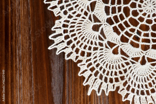 Corner of a vintage ivory crochet doily on a brown wooden table