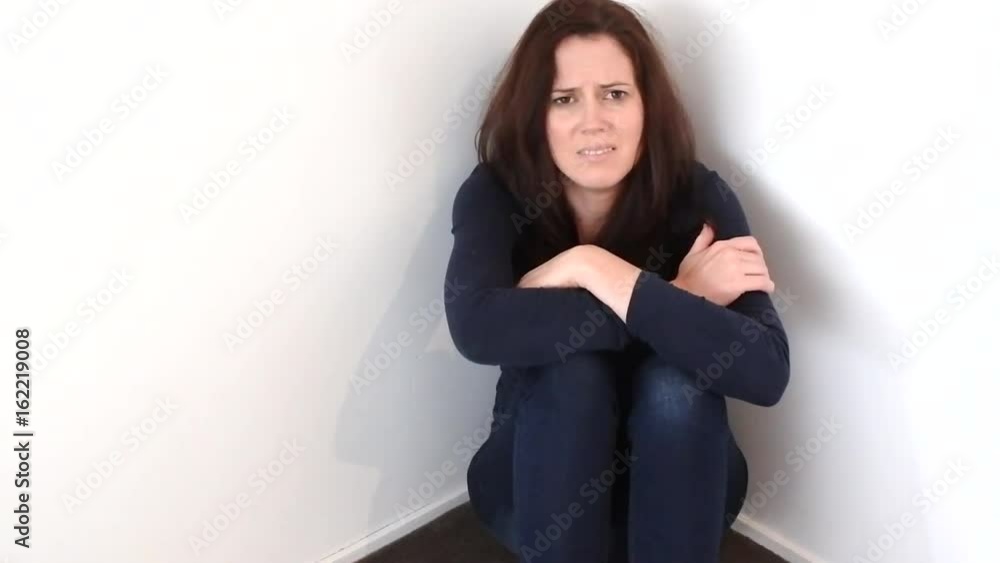 Young woman (age 30) crying on the floor in the corner of a room. Real people. Copy space. Young woman (age 30) crying on the floor in the corner of a room. Real people. Copy space.