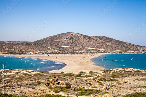 Fototapeta Naklejka Na Ścianę i Meble -  Beach between two seas. Beach between the islands of Rhodes and Prasonisi. Road across the sea. People practicing Kitesurfing. Colorful kites on the sea shore. Blue waves sea and sky.