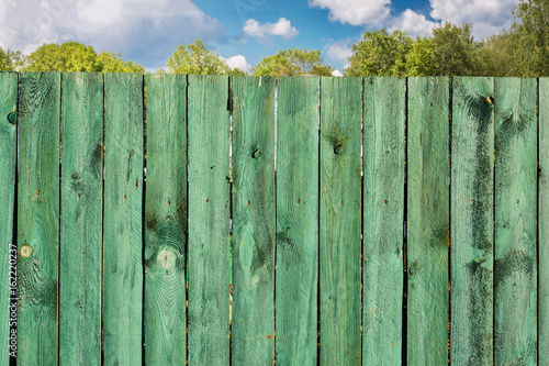 Old wooden turquoise fence and blue sky with clouds