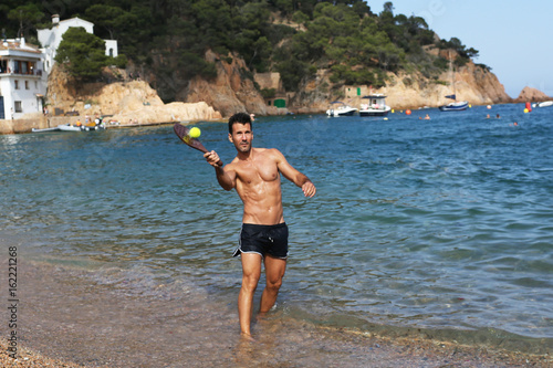 Sportlicher Mann mit Strand Schläger spielt am steinigen Strand photo