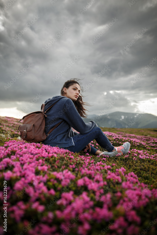 Flowers in the mountains. Shot of a young woman looking at the landscape while hiking in the mountains. Magic pink rhododendron flowers on summer mountain