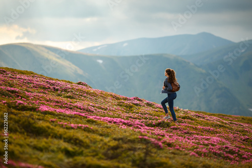 Shot of a young woman looking at the landscape while hiking in the mountains. Flowers in the mountains. Majestic flowers glowing by sunlight. Magic pink rhododendron flowers on summer mountain