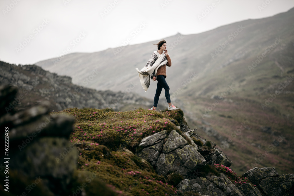 Young hipster woman hiker hiking on mountain trail. Travel concept. Traveler standing on top of a mountain. Hiker girl wrapping in warm poncho outdoor. Beautiful boho woman