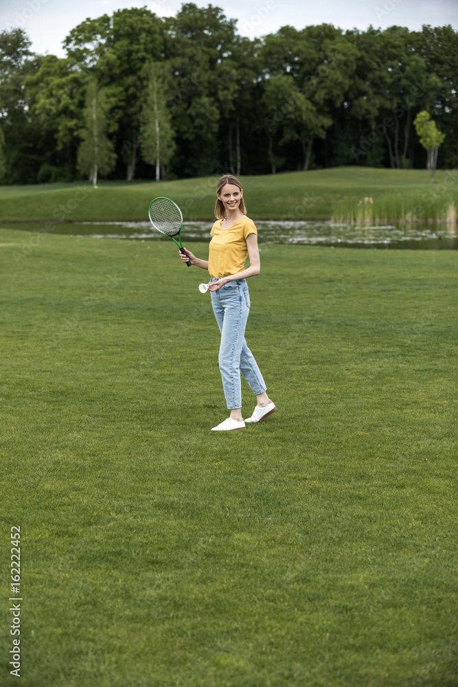 attractive caucasian woman playing badminton on green field in park