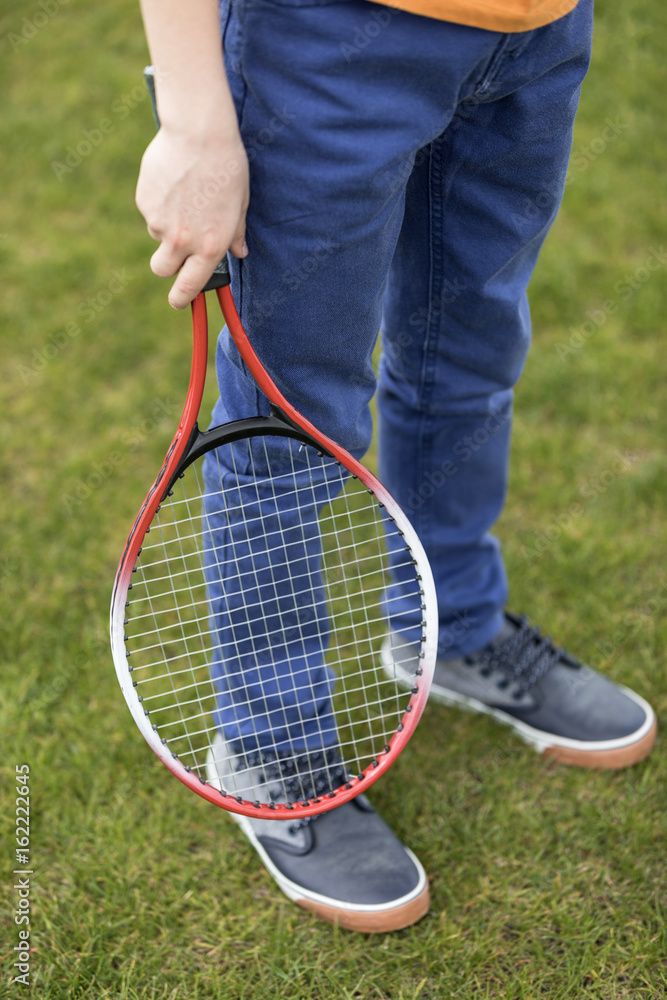 Cropped shot of boy holding badminton racquet while standing on green grass