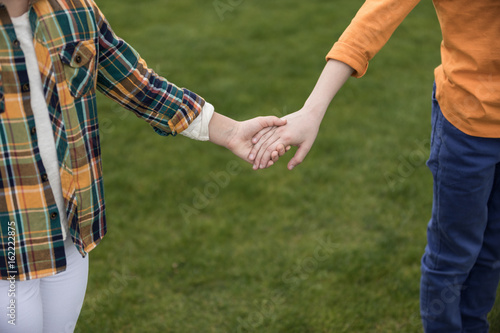 Cropped shot of two little children holding hands while standing on green grass