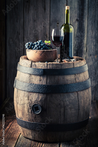 Red wine with fresh grapes on oak barrel