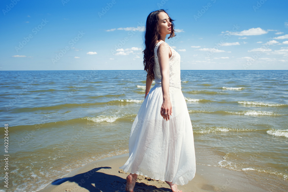Young beautiful brunette woman in white dress on the seashore Young beautiful brunette woman in white dress on the seashore