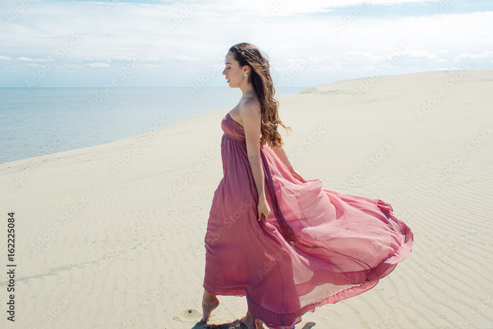 Woman in red waving dress with flying fabric runs on background of dunes Woman in red waving dress with flying fabric runs on background of dunes