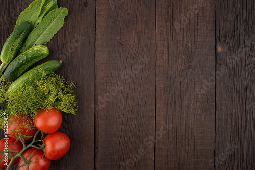 Tomatoes, cucumbers, dill and horseradish leaves on the old wooden background.