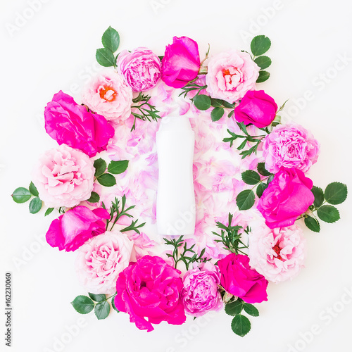 Round frame of pink roses, pink petals and shampoo on white background. Flat lay, top view. Floral pattern