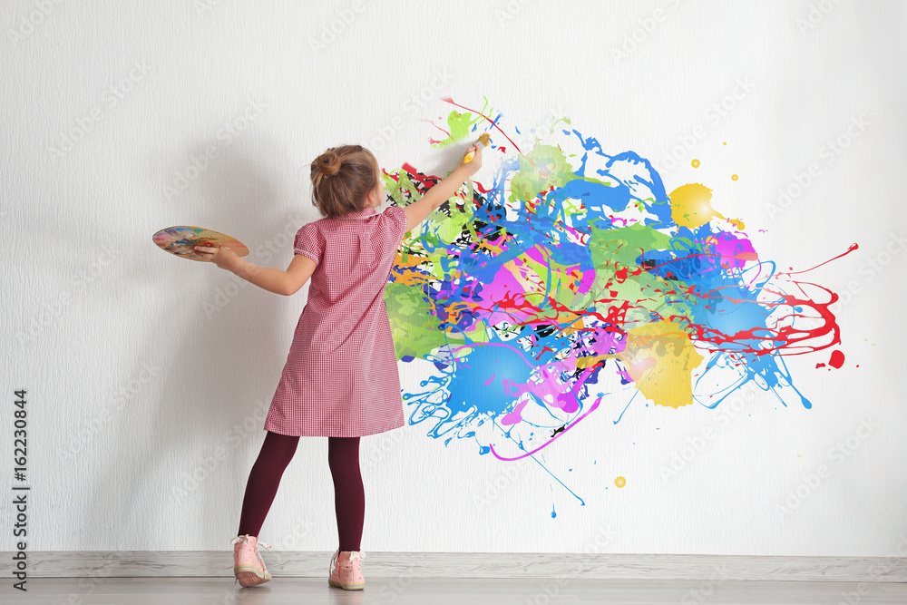 Fototapeta premium Cute little girl painting on wall in empty room