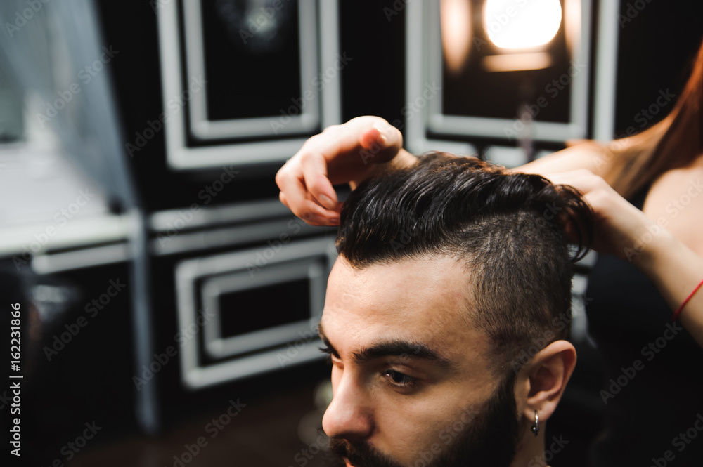 Fototapeta premium Master cuts hair and beard of men in the barbershop, hairdresser makes hairstyle for a young man