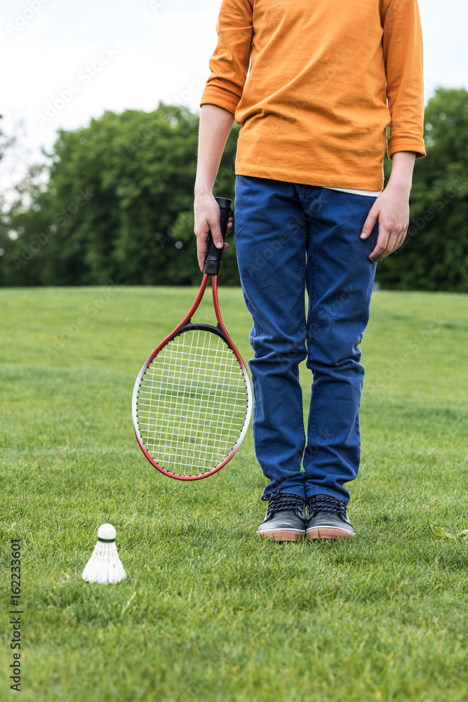 Cropped shot of little boy holding badminton racquet and standing on green grass with shuttlecock near by