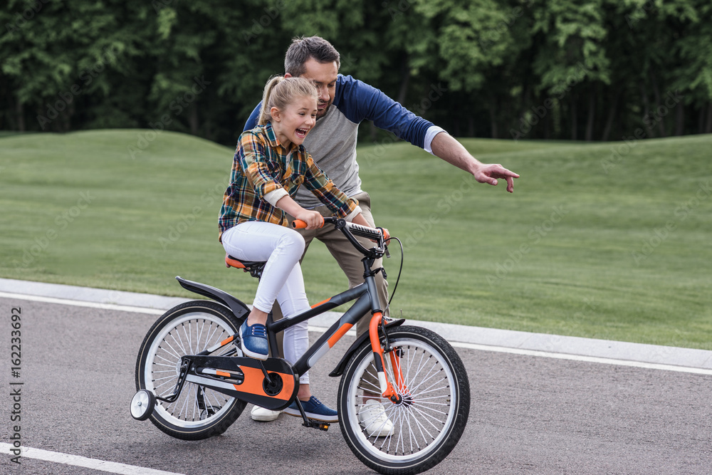 young father teaching his little daughter riding bicycle on asphalt road