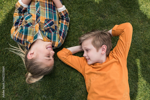 top view of little boy and girl looking at each other while lying on green lawn