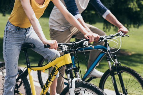 cropped shot of couple riding bicycles together in park