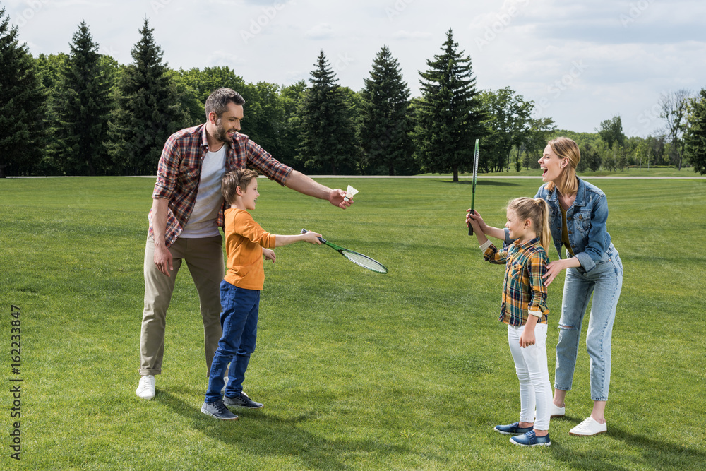 Parents teaching little kids how to play badminton outdoors