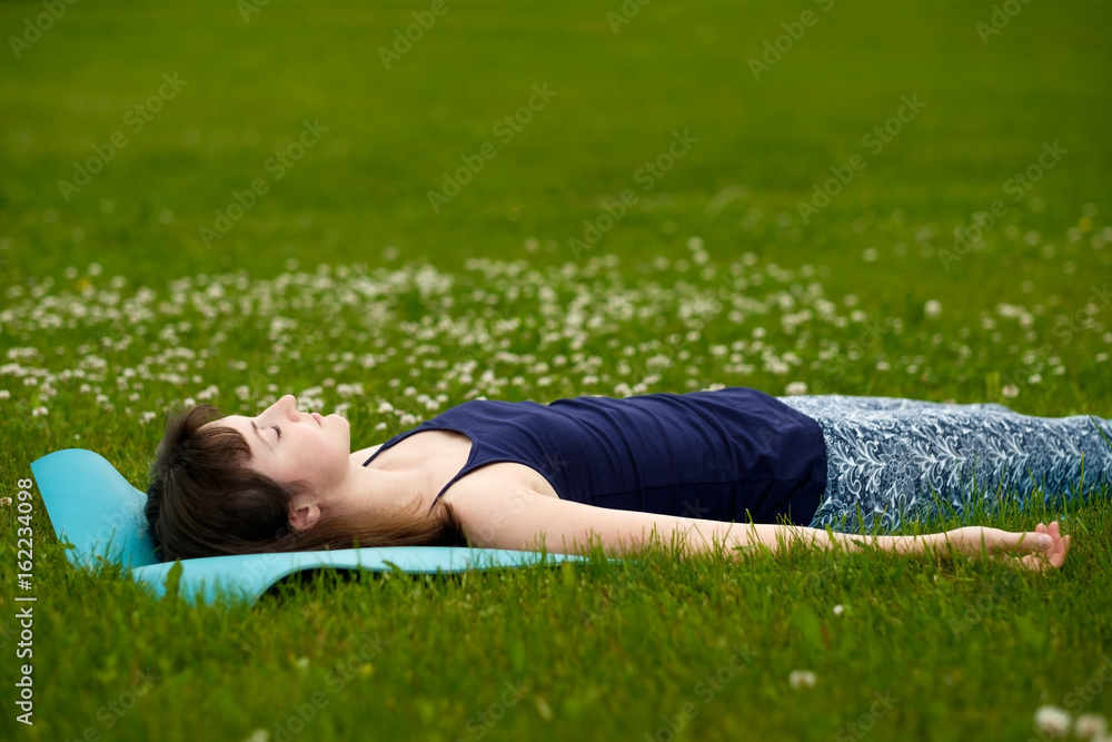 Girl doing yoga, meditating, Shavasana or corpse position in park on green grass Girl doing yoga, meditating, Shavasana or corpse position in park on green grass