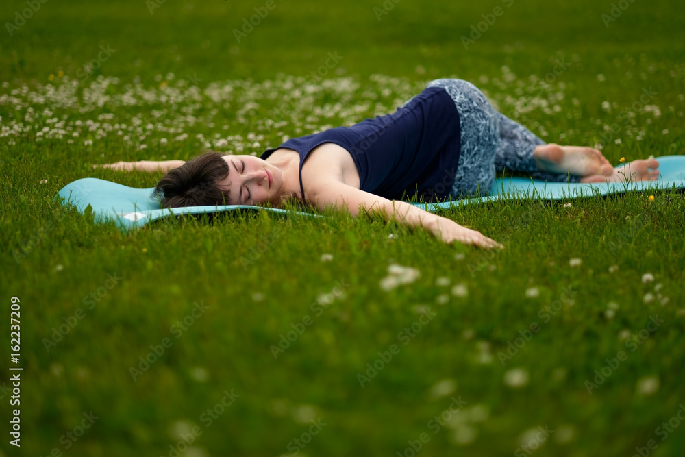 Beautiful caucaisan young woman working out outdoors on blue mat. Jathara Parivartanasana top view Beautiful caucaisan young woman working out outdoors on blue mat. Jathara Parivartanasana top view