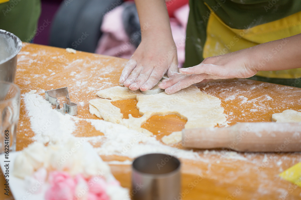 Cookery scene with female hands cutting cookies from raw dough with metal cutter on light brown table. Cookery scene with female hands cutting cookies from raw dough with metal cutter on light brown table.