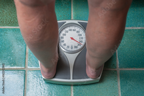 A severely overweight person weighing herself or himself on a bathroom scale photo