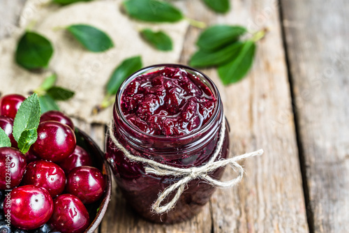 Cherry jam in jar and fresh cherries in a bowl, homemade preserves on rustic background