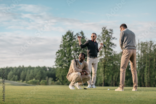 stylish multicultural friends spending time together while playing golf on golf course