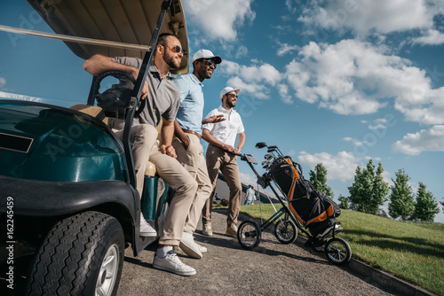 Canvastavla group of smiling friends standing near golf cart and looking away