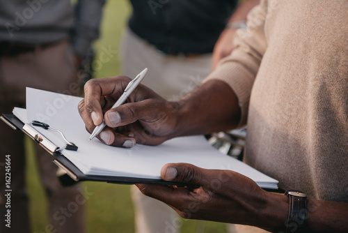 cropped view of african american man writing something on paper in clipboard