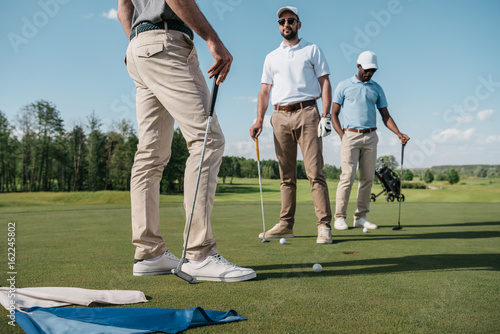 professional golfers talking while standing and holding clubs on green pitch