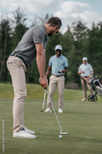 golfer aiming to hit a ball with club during play with his friends at daytime