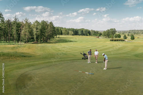 multiethnic group of sportsmen playing golf on green fairway at daytime