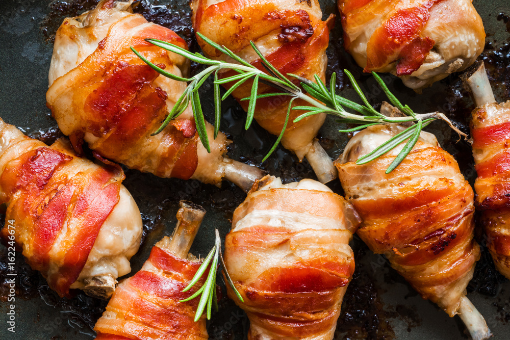 Oven roasted bacon wrapped chicken drumsticks in a black baking pan