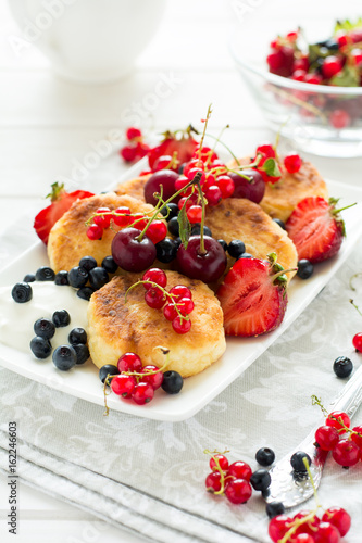 Healthy breakfast: cheese pancakes with sour cream and fresh ripe berries on white wooden table. Selective focus 