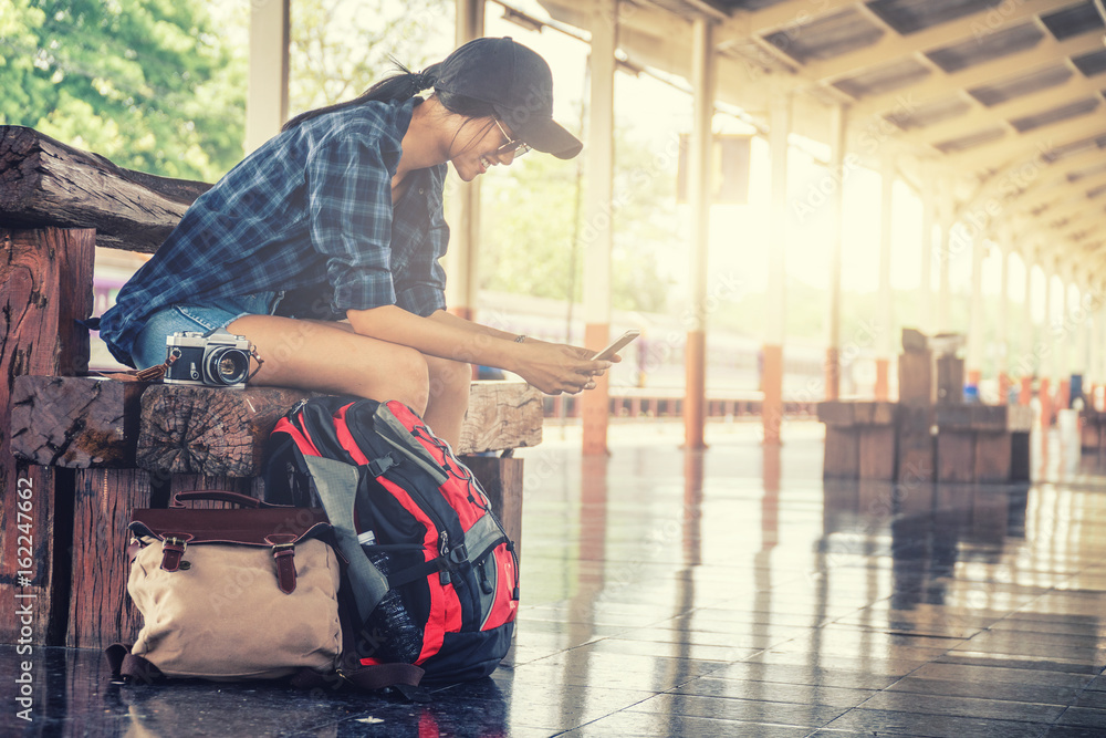 alone woman sitting and playing smart phone with travel accessories,travel accessories and backpacker concept,sun flare effect and vintage tone.