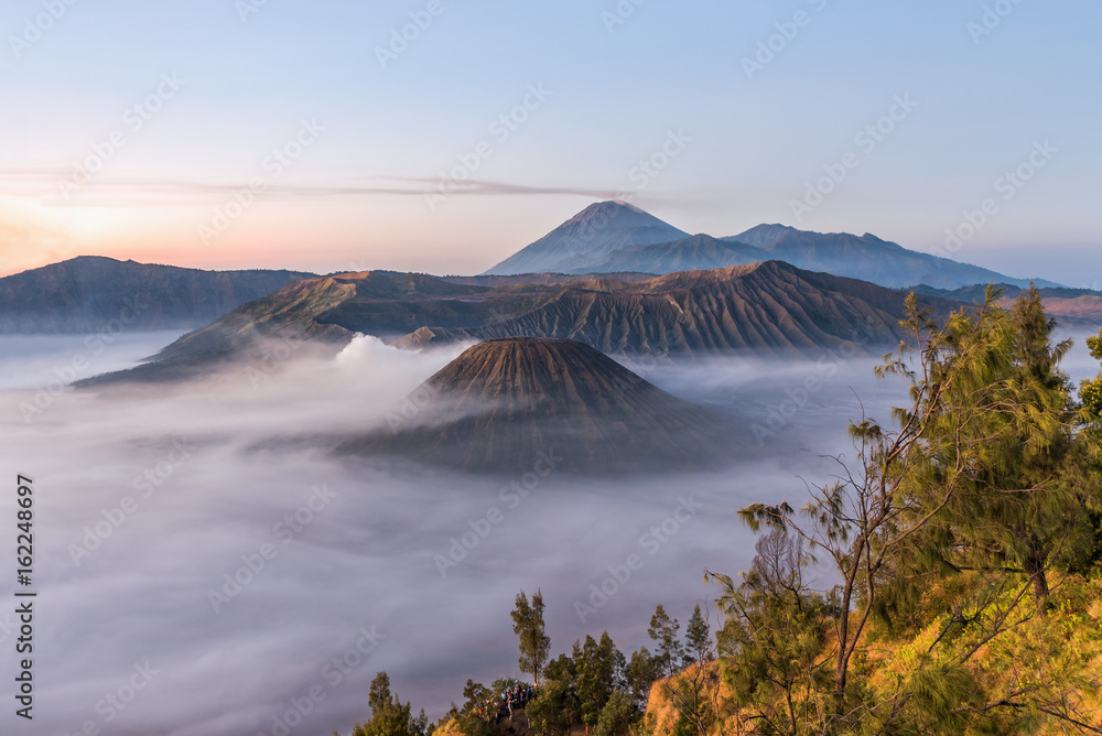 Fog covered Bromo mountain valley at sunrise.