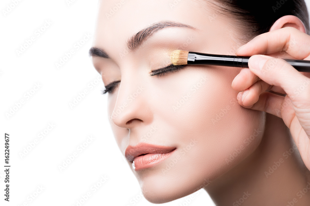 Makeup artist using brush to apply eye shadow on face of woman