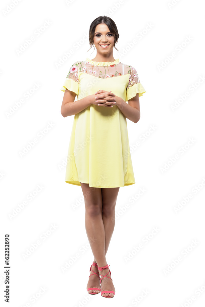 Cute pretty smiling woman in yellow dress standing with clasped hands looking at camera. Full body length portrait isolated on white background. Cute pretty smiling woman in yellow dress standing with clasped hands looking at camera. Full body length portrait isolated on white background.