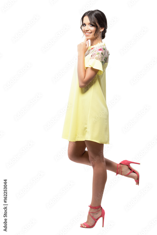 Gorgeous woman in yellow short summer dress leaning on the wall smiling at camera. Full body length portrait isolated on white background. Gorgeous woman in yellow short summer dress leaning on the wall smiling at camera. Full body length portrait isolated on white background.