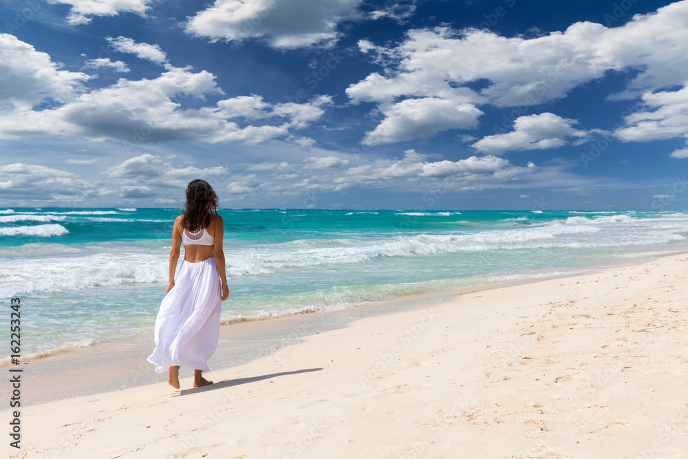 Frau in weißem Kleid läuft am Strand der Karibik