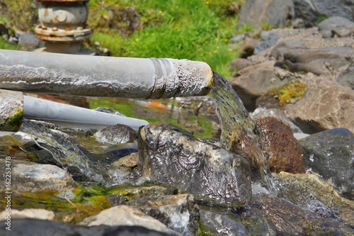 End of a rusty pipeline with a hot geothermal water flowing into the natural creek in the Icelandic natural park 