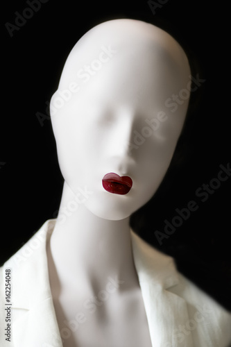 White mannequin without eyes and with red lips on a black background