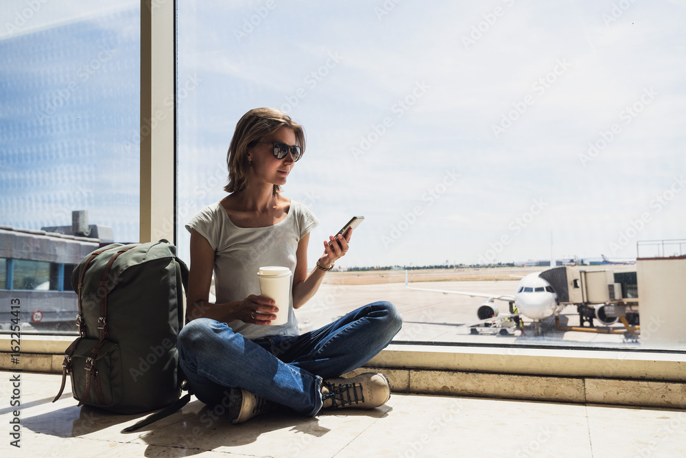 Young woman in the airport, using smart phone and drinking coffee, travel, vacations and active lifestyle concept