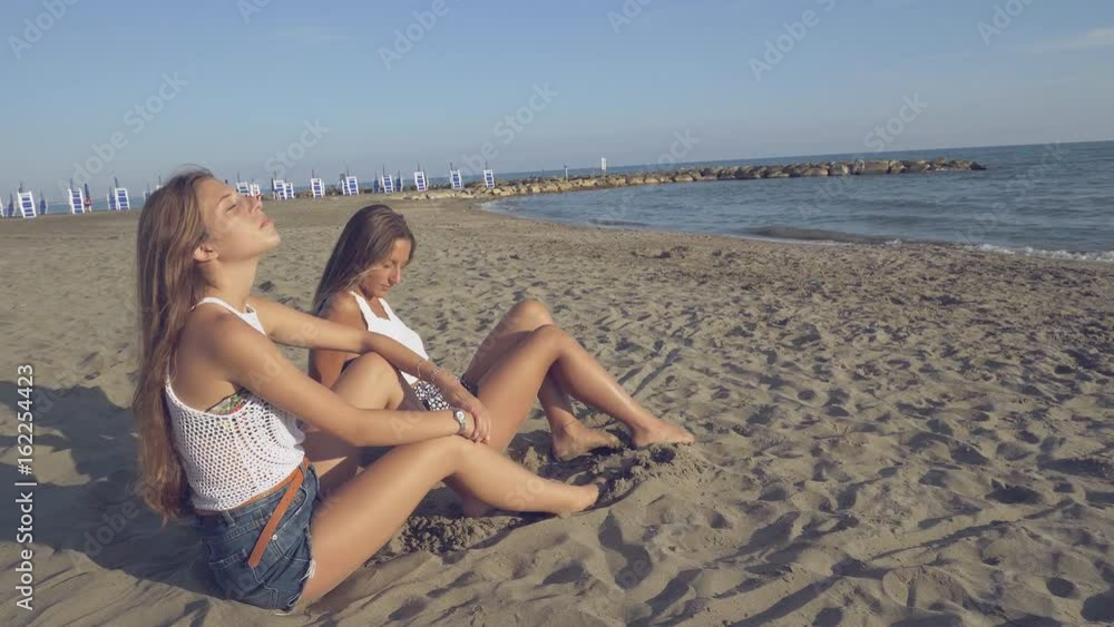 Cute girls on beach enjoying the sun in front of the ocean 4K slow motion wide shot Cute girls on beach enjoying the sun in front of the ocean 4K slow motion wide shot