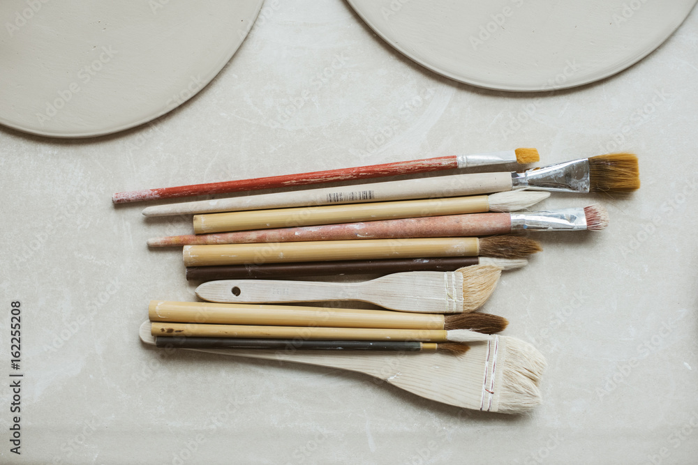 Fototapeta premium Top view on different rustic brushes with wooden holders for ceramic and workpieces for handmade plates
